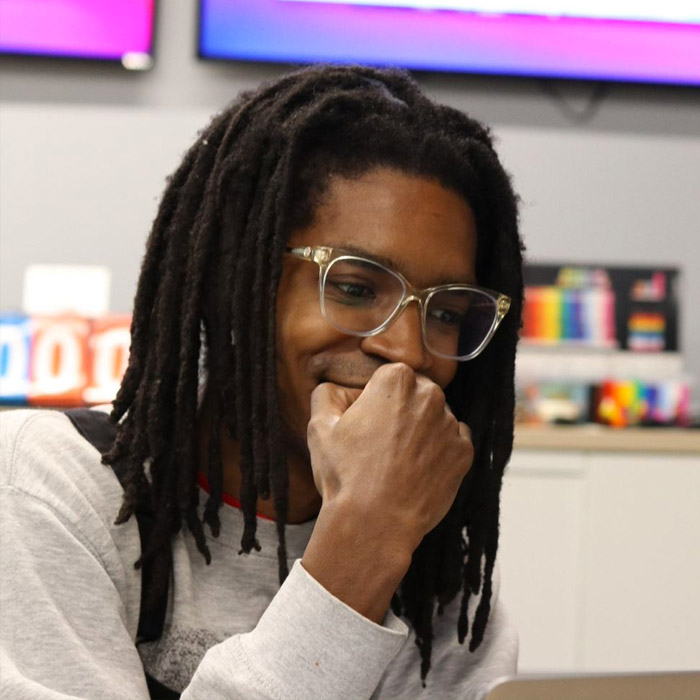 Man in glasses, working on his laptop and grinning.