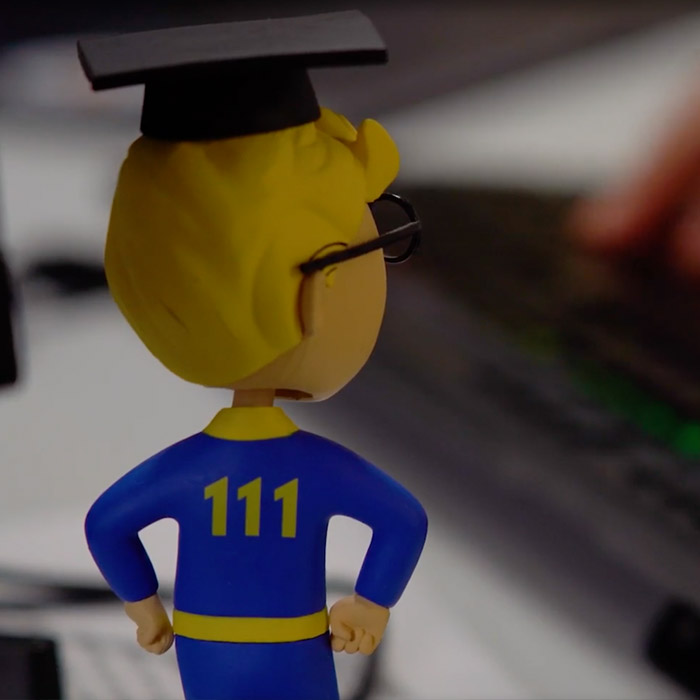 Bobble-head in glasses and a graduation cap facing away from the camera. Wearing blue and yellow with the number 111 on the back of his shirt.