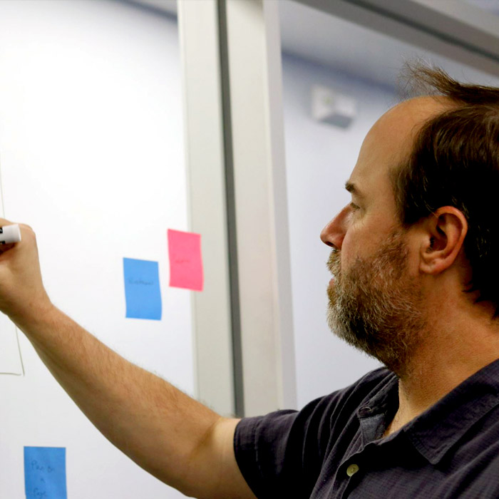 Man writing on a white board, outlining engineering strategy and design.
