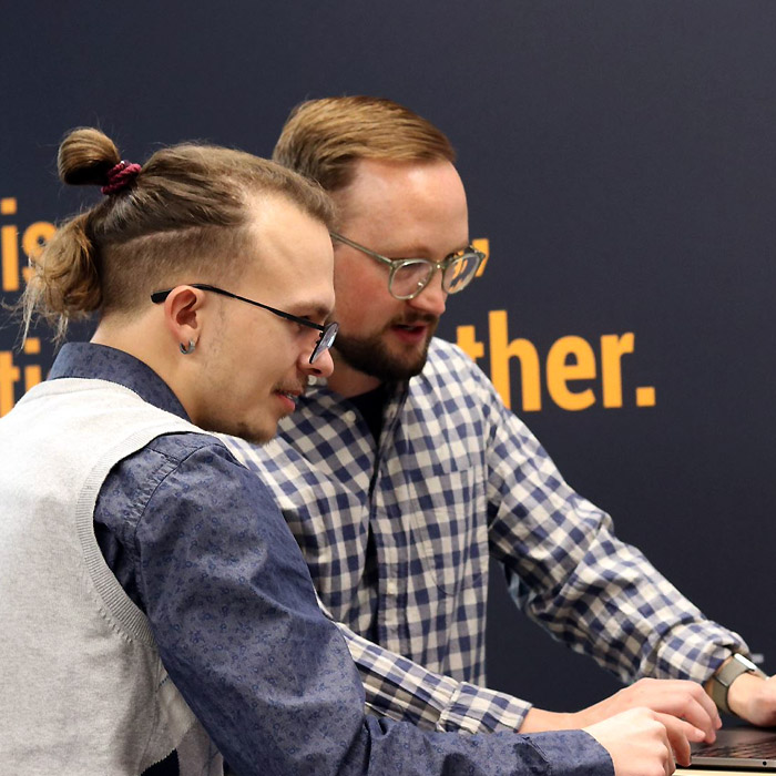 Two men in glasses in conversation, standing and working on one laptop in collaboration. 