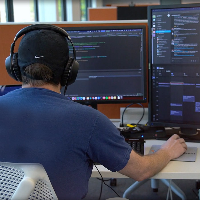 Man working at his desk on his computer. He is wearing headphones on and is writing code.
